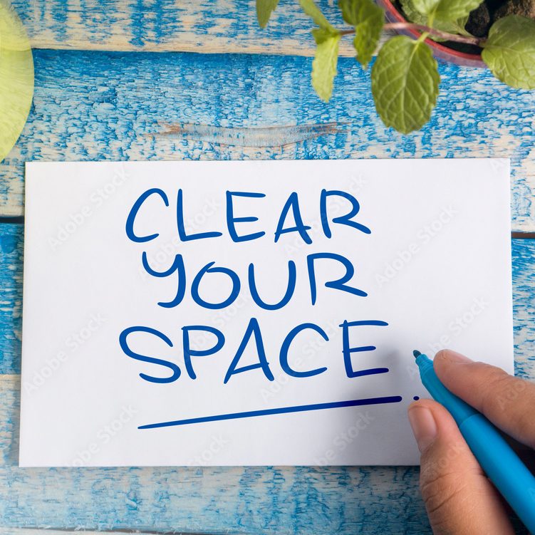 Hand schreibt "CLEAR YOUR SPACE" auf ein Blatt Papier vor einer blauen Oberfläche.